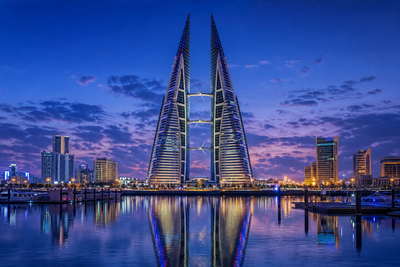 Bahrein: zeiltorens van het Bahrain World Trade Center in Manama vlechten marineturbinebladen in kobaltblauw schemerglas, specerijentocht onder de boog van Bab al-Bahrain richting dhow-kielzog bij parelwinkels in Muharraq en zeedijken van Qal'at al-Bahrain die stoom van tannur-brood vangen in de hero - achtergrond voor telbriefjes voor parelgewicht in Bahreinse dinar (BHD), weeglabels voor halwa-showq-zakken en gevouwen parkeerbonnen voor het circuit van Sakhir.