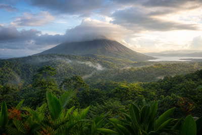 Costa Rica: perfecte kegel van de vulkaan Arenal die mistkam door het regenwoud bij La Fortuna vlecht onder tropische cumulus, jadegroene bromelia-nevel van het wolkenbos van Monteverde naar gouden streeklijnen op de Stille Oceaan in Tamarindo en koffierookdamp van Mercado Central in San José met perkselstroken uit Tarrazú in de hero - achtergrond voor soda-briefjes in Costa Ricaanse colón (CRC), gevouwen harnas-stempels bij zip lines in het kruin en bonnetjes voor stomende casado-borden.