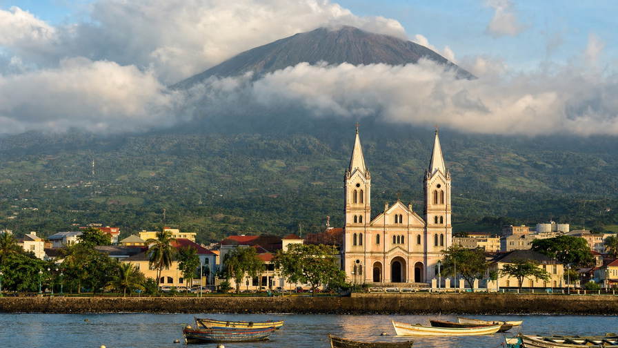 Equatoriaal-Guinea: kathedraaltorens in Malabo boven havennevel in de Golf van Guinee, wolkendek op de Pico Basilé boven cacaodroogschuren op Bioko en grillstallen met zeevruchten op de boulevard van Bata langs Rio Muni in de hero - achtergrond voor fufu-met-vis, hotelcafé aan het plein en CFA-prijzen voor gedeelde taxi's langs de kust.