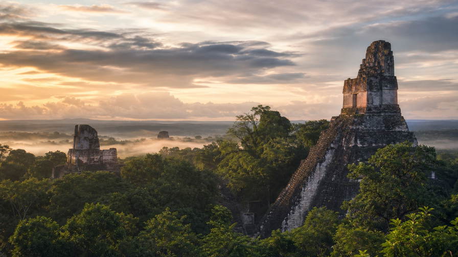 Guatemala: kalkstenen lint van Tikal I dat nevelkam door de jungle van Petén vlecht onder equatoriale cumulus, smaragdgroene nevel van het Atitlán-meer aan vulkaanranden naar kasseien van vulkanisch gesteente in Antigua en gestreepte textielmarkiezen in Chichicastenango met pergamentstof van koffiemolens in Huehuetenango in de hero - achtergrond voor huipil-marktbrieven in quetzal (GTQ), gevouwen stempels voor daklading op chicken buses en weegbriefjes voor microlot-koffiekersen.