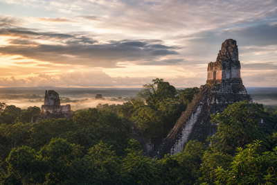 Guatemala: kalkstenen lint van Tikal I dat nevelkam door de jungle van Petén vlecht onder equatoriale cumulus, smaragdgroene nevel van het Atitlán-meer aan vulkaanranden naar kasseien van vulkanisch gesteente in Antigua en gestreepte textielmarkiezen in Chichicastenango met pergamentstof van koffiemolens in Huehuetenango in de hero - achtergrond voor huipil-marktbrieven in quetzal (GTQ), gevouwen stempels voor daklading op chicken buses en weegbriefjes voor microlot-koffiekersen.