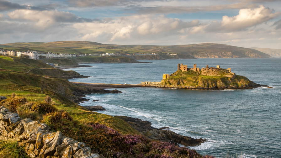 Isle of Man: graniet-vlecht van de promenade van Douglas over haven-chopbanden van de Ierse Zee onder handels-cumulus, kopernevel van het Snaefell-moor naar perkamentstapels bij Peel Castle en lint van Laxey-glen bij het waterrad Lady Isabella plus weidegruis van Manx Loaghtan-schapen in de hero - achtergrond voor GBP markt-streepjes met Manx-pond-sterling-pariteit-stroken, EUR Ierse-Zee-veerboot-charter-stempelvouwen bij ponton-stapels van Douglas Sea Terminal en rook-haring-weegbriefjesbanden in Ramsey-baai.