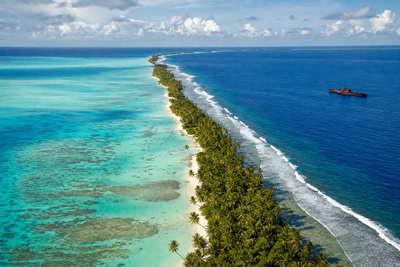 Kiribati: turquoise atolband rond Tarawa die dubbele spiegel van oceaan en lagune vlecht onder passaat-stratus, roestkleurige wraksilhouetten bij Betio naar geweven mattenstallen in Bairiki kopra-zakpiramides en zilveren strepen van noddy-vlucht boven het rif in de hero - achtergrond voor marktzettels in Australische dollars (AUD), diesel-buitenboordliterbonnen en weegbriefjes voor kopra naar de buiten-eilanden.