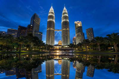 Maleisië: roestvrijstalen ruggengraat van de Petronas-tweeling die kobaltblauw spiegelglas van het KLCC-bassin vlecht in het blauwe uur, pastelkleurige winkelhuizen in George Town op Penang richting nasi lemak-stoom op bananenblad op Jonker Walk bij nacht in Malakka en wolkencolliers rond de top van Kinabalu op Borneo in de hero - achtergrond voor streepjes bij spiesjes op nachtmarkten in Maleisische ringgit (MYR), grammenstickers voor Musang King-durian en gevouwen tickets voor boomkroonpaden.