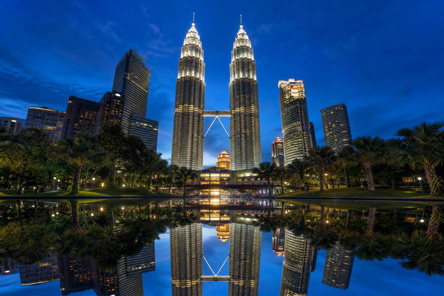 Maleisië: roestvrijstalen ruggengraat van de Petronas-tweeling die kobaltblauw spiegelglas van het KLCC-bassin vlecht in het blauwe uur, pastelkleurige winkelhuizen in George Town op Penang richting nasi lemak-stoom op bananenblad op Jonker Walk bij nacht in Malakka en wolkencolliers rond de top van Kinabalu op Borneo in de hero - achtergrond voor streepjes bij spiesjes op nachtmarkten in Maleisische ringgit (MYR), grammenstickers voor Musang King-durian en gevouwen tickets voor boomkroonpaden.