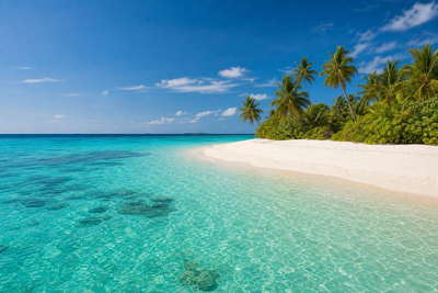 Maldiven: jade-tot-saffier lagunemotief boven koraalondiepten, kokospalmen op een zandomzoomd eiland en krijtwitte ondiepten onder passaat-stapelwolken in de hero-foto - visuele intro voor vergelijkingen van resort-atol- en Malé-bevoorradings-supermarkt-, horeca- en guesthouse-huur.