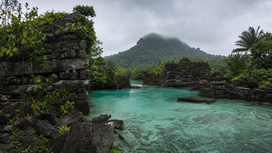 Micronesia: jadeglazen lagunevlaktes bij Chuuk die silhouetten van oorlogswrakken in koraalbloemen onder grijze stratus vlechten, nevelige basaltring van Nan Madol op Pohnpei naar betelnootpiramides in de schaduw van de Colonia-markt en glans van kalkstenen rai-schijven in ondiepe Yap-lagune in de hero - achtergrond voor briefjes voor wrakduiken in US-dollars (USD), gevouwen dekstickers op schepen tussen de staten en weegbriefjes voor gewicht aan sakau-kavawortel in pond.