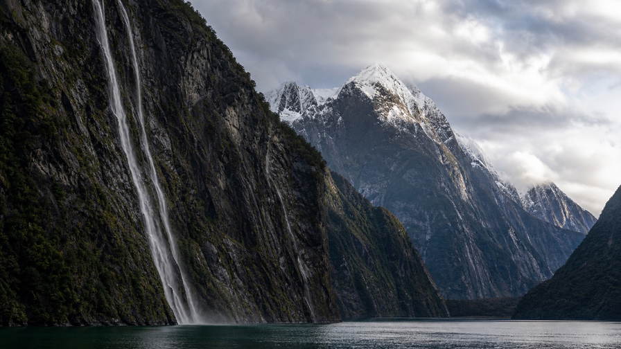 Nieuw-Zeeland: sneeuwrug van de Southern Alps die Milford Sound-mist vlecht langs zwarte wanden van water, gloed van tussock-ruggen bij Queenstown, zwavelstoom over Rotorua naar staalkabels van de kabeltram in Wellington en pinot-noir-wijnrijen in Central Otago in de hero - achtergrond voor hutboekingsbriefjes in Nieuw-Zeelandse dollars (NZD), dekstempels van de Interislander-veerboot door de Cookstraat en weegbriefjes voor honingpotjes op de boerenmarkt.