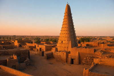 Niger: spiraalvormige lemen minaret in Agadez bij de poort naar het Aïr-massief, Fulani-vee langs droge rivierbeddingen en nevelige kades van de Niger achter Niamey in de hero - achtergrond voor gierstzakken op Wadata, drie suiker-theeglazen en kantinebonnen op truckersparkeerplaatsen.