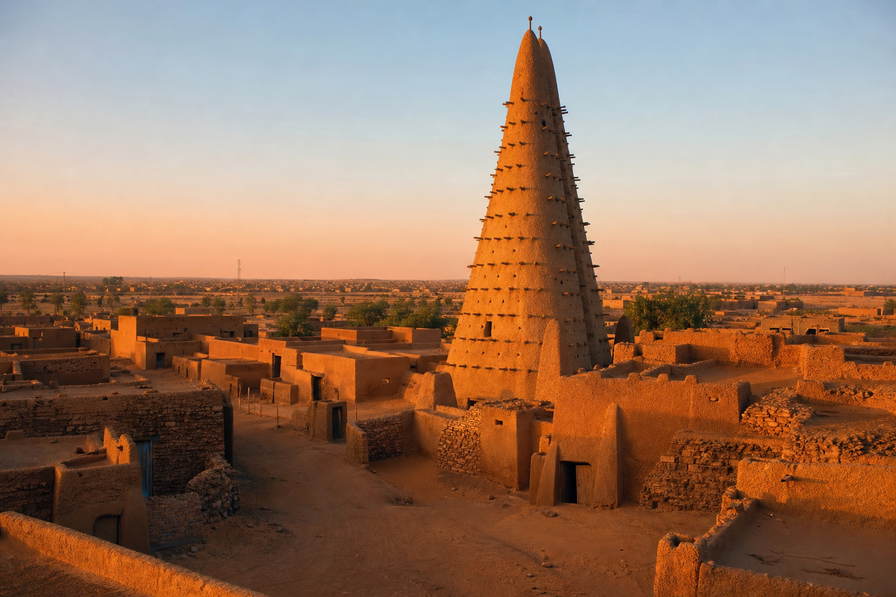 Niger: spiraalvormige lemen minaret in Agadez bij de poort naar het Aïr-massief, Fulani-vee langs droge rivierbeddingen en nevelige kades van de Niger achter Niamey in de hero - achtergrond voor gierstzakken op Wadata, drie suiker-theeglazen en kantinebonnen op truckersparkeerplaatsen.