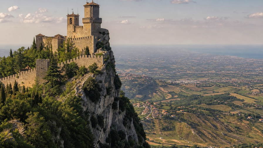San Marino: kalkstenen klifkruinen vlechten kanteelmuur-schaduwen, terracotta-dakstapels klimmen Titano-achtige ruggen en Adriatische zilvernevelbanden in de hero-foto - visuele intro voor EURO-kassabonnen in duty-vriendelijke winkels, pasta-truffel-horeca in het heuvelstadje en huur-ladders voor terrasgasten in Borgo.