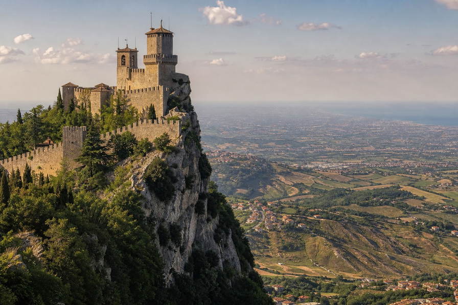 San Marino: kalkstenen klifkruinen vlechten kanteelmuur-schaduwen, terracotta-dakstapels klimmen Titano-achtige ruggen en Adriatische zilvernevelbanden in de hero-foto - visuele intro voor EURO-kassabonnen in duty-vriendelijke winkels, pasta-truffel-horeca in het heuvelstadje en huur-ladders voor terrasgasten in Borgo.