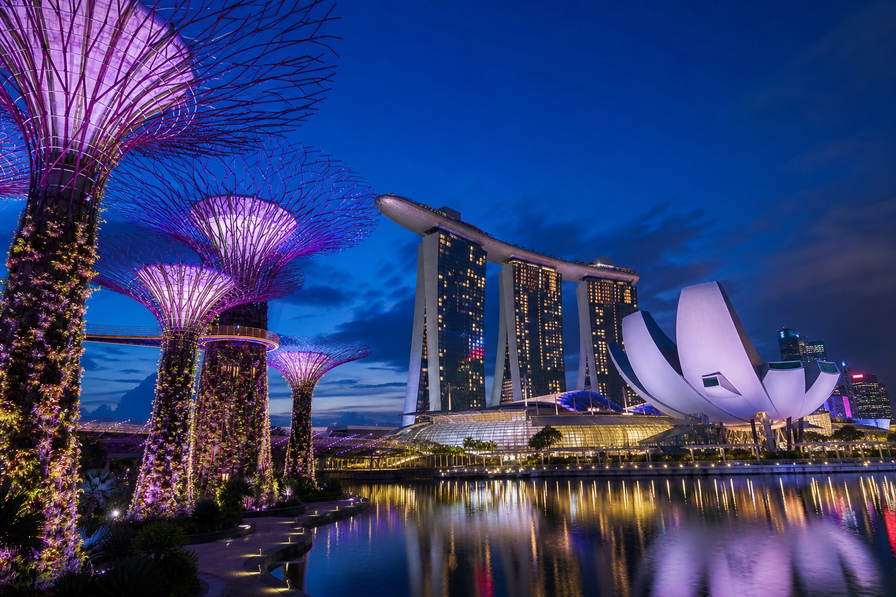 Singapore: verticale supertree-tuinen in Marina Bay die paarse lasernevel van lotusblaadjes van ArtScience Museum vlechten, neonrimpelingen bij Clarke Quay richting satérook van hawkercentra onder wasgoed-geometrie aan HDB-flats en robijnrode avondstrepen van de kabelbaan naar Sentosa in de hero - achtergrond voor jetons bij hawkerkramen in Singaporese dollar (SGD), gevouwen bonnen voor kopi-o met sokfilter en stapels EZ-link-opwaardeerstrookjes.