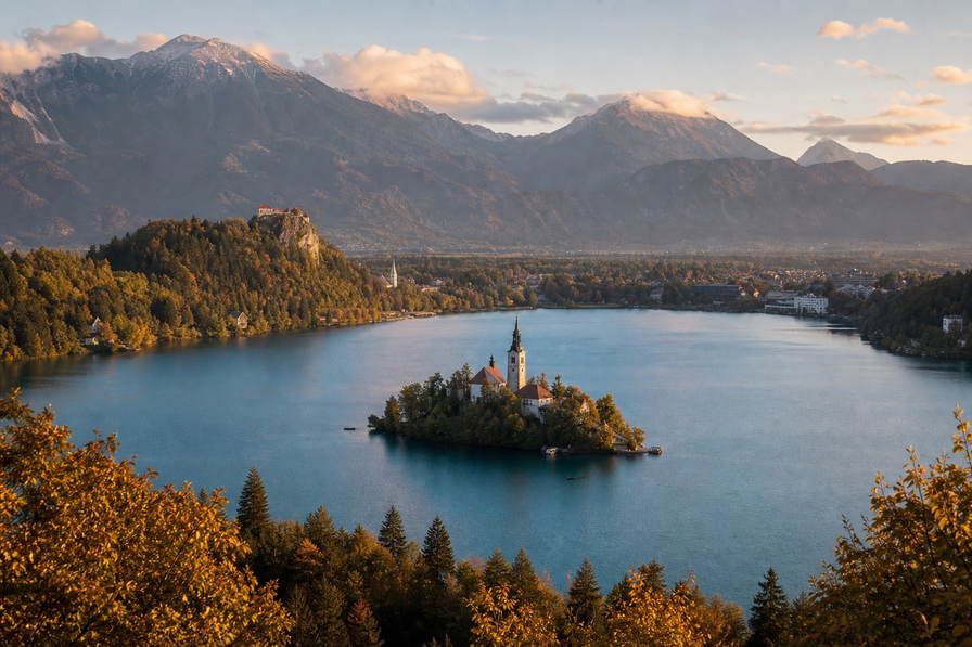 Slovenië: kerk-eiland op smaragdgroen Bledmeer, Julische Alpen-passen en Karst-wijngaarden in de banner - scène voor kranjska-klobasa-toonbanken, grottickets en fietsdeelpassen in Ljubljana.