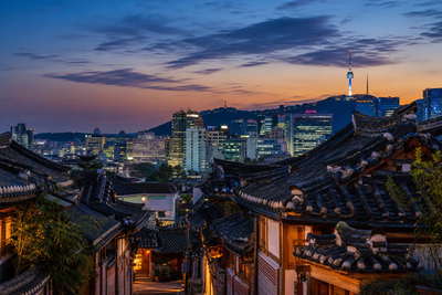 Zuid-Korea: stalen naald van de N Seoul Tower die neonparabelstapels over de Han-spiegel vlecht onder avondstratus, gebogen hanok-dakpannenscherm in Bukchon naar stoomdak van straateten in Myeongdong en ijsglans bij vis in Jagalchi, Busan in de hero - achtergrond voor bonnen van T-money-taps in won (KRW), gevouwen snackkar-stempels op de KTX en weegbriefjes voor jjimjilbang-kastslotbanden.