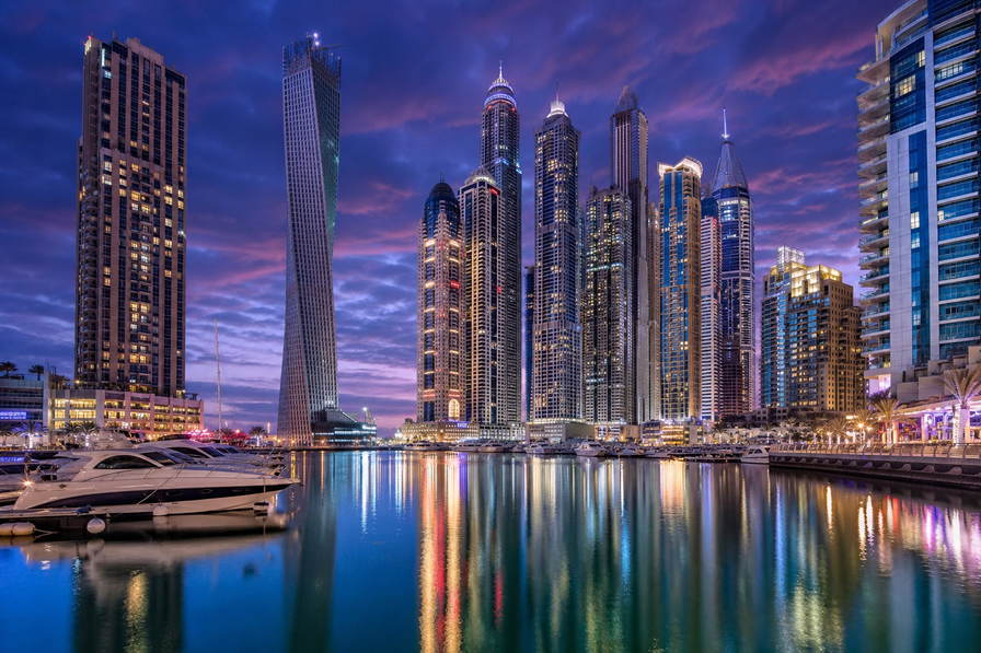 Verenigde Arabische Emiraten: glazen gevels van Dubai Marina die jachtkielzicht dubbelen in het blauwe uur, parelmoer-rimpelingen van koepels in Abu Dhabi richting LED-gloed van de goudsouk in Deira en nevelbanden van duin naar beton op Saadiyat in de hero - achtergrond voor Salik-tolchipafdrukken in VAE-dirham (AED), grammenbriefjes voor 22-karaats gouden kettingen en stapels aankruisvakjes op vrijwaringsformulieren voor woestijnsafari-duinritten.