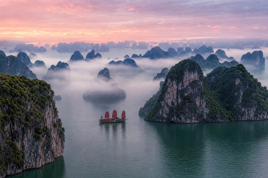 Vietnam: kalkstenen eilanden in Ha Long Bay die jadegetij-vingerafdrukken vlechten door zijdeachtige ochtendmist, pho- en druppelkoffiestoom bij Train Street in Hanoi richting draakboot-kielzicht met lotusblaadjes op de Parfumrivier in Hue en auberginekleurige lantaarnreflecties op het water in Hoi An in de hero - achtergrond voor streepjes op pho-kraampjes in Vietnamees dong (VND), weeglabels voor cashewnoten in bulk en kartonstapels voor peddelhuur op de drijvende Mekong-markt.