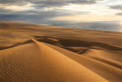 Westelijke Sahara: Atlantische duinenkam vlecht Laayoune golfbanden onder handelsstapelwolken, koper-jade nevel van Dakhla-lagune naar Smara-plateau en perkamentstapels aan de kade, erglint in kustmist-haar plus stof van de weg naar Aousserd in de hero - achtergrond voor MAD souk-streepjes, EUR veerboot-charter-stempelvouwen bij havenglijkais in Dakhla en USD sardien-weegbriefjesbanden.